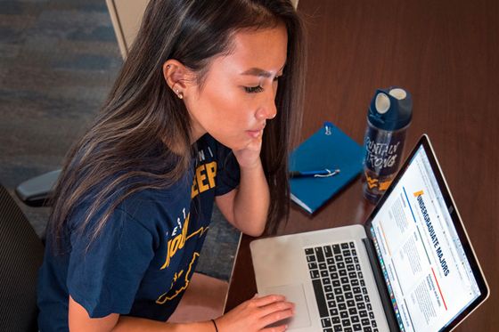 Female student wearing a WVU t-shirt working on a laptop.