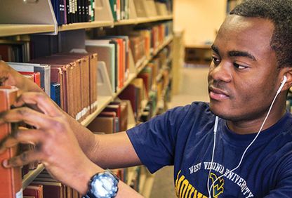 WVU student getting book from library shelf.